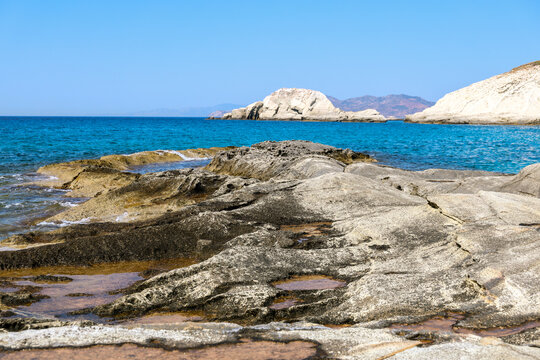 Rocky shoreline and turquoise sea under a clear blue sky on the island of Milos, Greece.