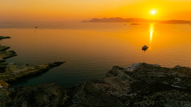 A golden sunrise over the Aegean Sea near Milos, Greece, with a boat floating on calm water.