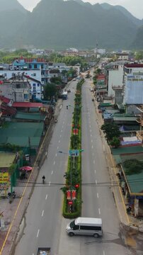 Vertical screen Shuttle Vehicle In Phong Nha. Overhead Shot Of Shuttle Van Crossing Median In Phong Nha Area. Aerial Perspective Of White Shuttle Van Passing Over Central Median In Phong Nha