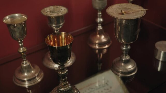 Group of silver liturgical chalices and ciboria beside book on red background
