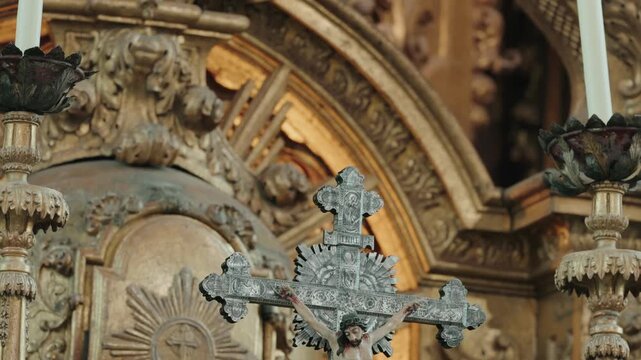 Ornate silver crucifix with Christ figure set against a gilded carved Baroque church altarpiece