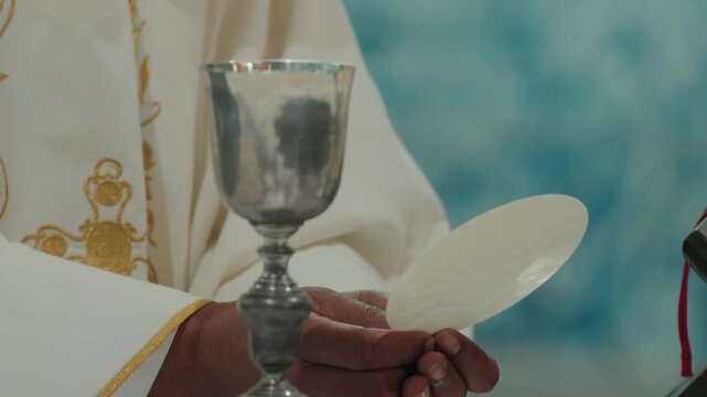Priest in white vestments raising communion host during the Eucharist at Mass