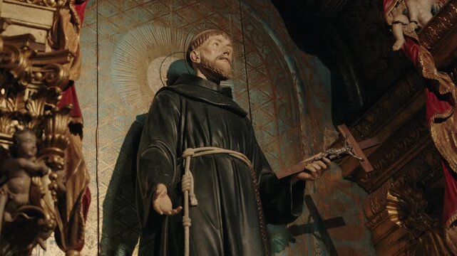 Carved statue of a Franciscan friar saint in a habit holding a crucifix in a gilded church altar