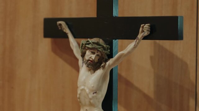 Carved crucifix with a Christ figure and crown of thorns on a dark cross against a wooden wall