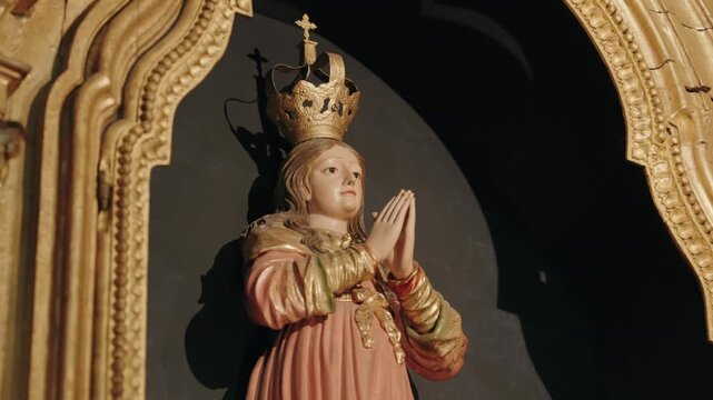 Statue of a crowned Virgin Mary with praying hands set against a gilded Baroque church altar