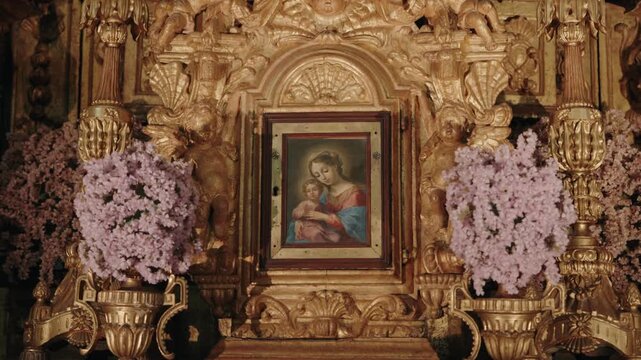 Framed Madonna and Child painting set in an ornate gilded Baroque altar with lilac flowers in Portugal