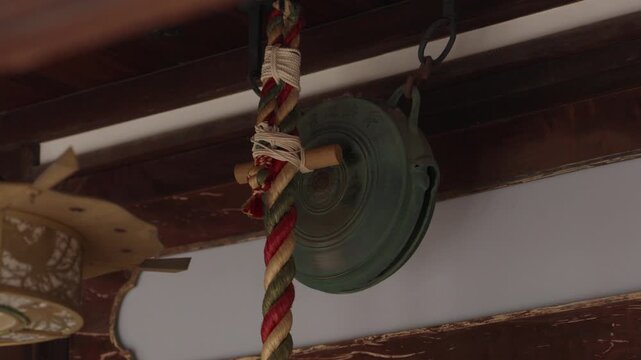Weathered bronze bell and thick colourful braided rope hanging under the eaves of a Japanese shrine