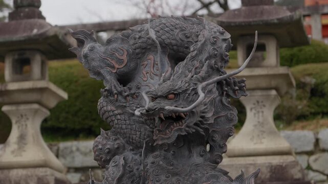 Ornate bronze dragon statue on a stone temizuya purification fountain among stone lanterns at a Japanese shrine