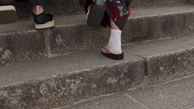 Feet in white tabi socks and traditional sandals walking up weathered mossy stone steps