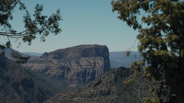 Layered rock butte in Morocco rising above wooded canyon slopes framed by juniper trees