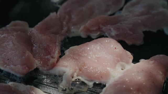 Fork turning thin pale meat slices searing on a dark griddle pan