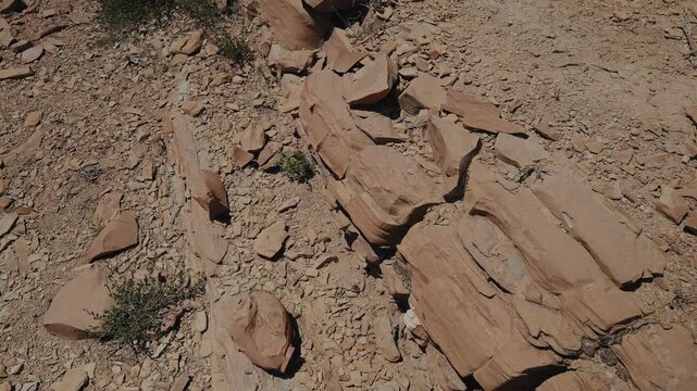 Layered red sandstone slabs and loose stones on a dry sunlit hillside in Morocco