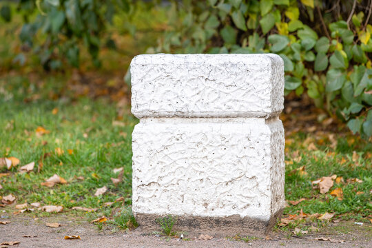 Rough white textured stone block resting on green grass beside a leafy hedge as a simple outdoor object