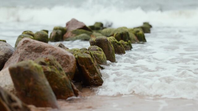 Wooden groyne and protective rocks on sandy beach. Seascape with breakwater extending into stormy sea. Erosion control structure on coastline. Natural scenery for travel concept.