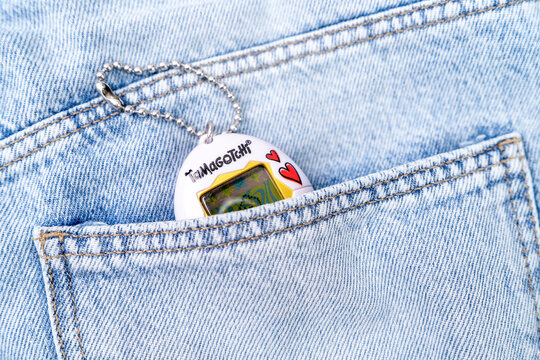 Bar, Montenegro: February 6, 2026: Retro white tamagotchi virtual pet toy on keychain clipped to light denim jeans pocket, nostalgic nineties childhood gaming lifestyle concept