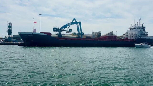 Cargo vessel docked at Poole Harbour featuring loading crane, commercial shipping operations, calm water, and working harbor in Dorset