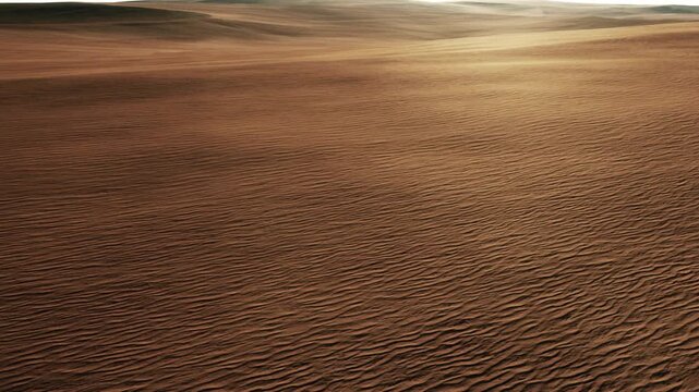 Wide view of sand dunes in a desert during the afternoon. The light creates patterns on the surface of the sand. There are no plants or animals visible in this area.