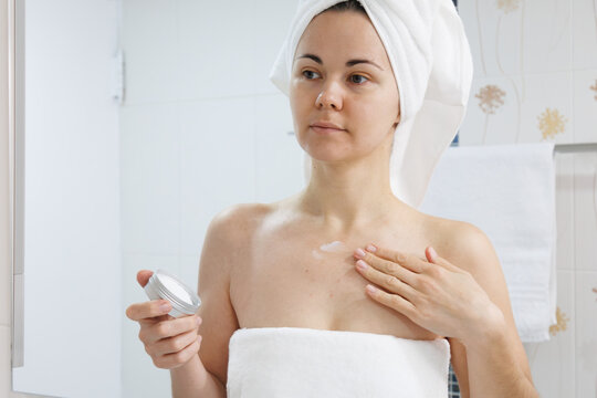 Woman applying moisturizing cream to the neck and decollete after a shower. Daily skincare, home beauty routine, cosmetics, self care, healthy skin, body care, and personal hygiene.