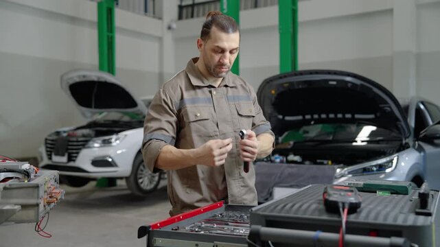 Professional automotive mechanic organizing tools before performing electric vehicle maintenance in a modern repair workshop. Automotive service, technical preparation, and professional repair concept