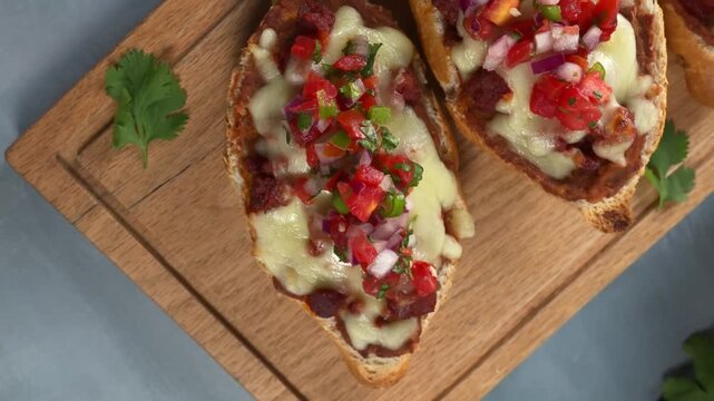 Mexican molletes with melted cheese and pico de gallo on wooden cutting board, close up