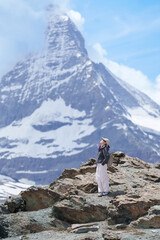 Naklejka premium Woman Tourist Exploring Zermatt, Switzerland in summer. Happy Hiker Standing on Rock along Hiking Trail with Matterhorn, Swiss Alps, Famous Europe Landmark, Hiking Attraction and Travel Destination