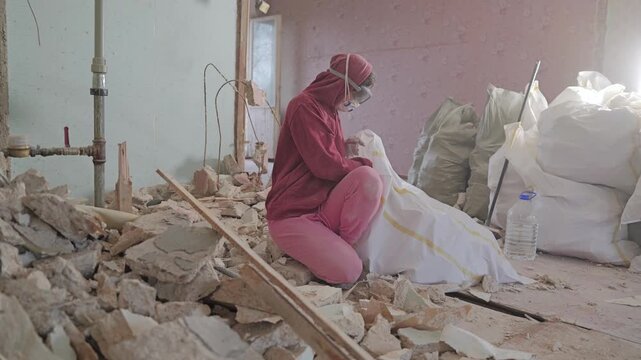 Woman wearing respirator fills debris bags during dusty apartment demolition
