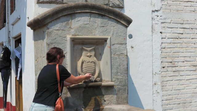 A Woman Walking Near Pila del Tecolote, Historic Stone Water Fountain In Tapalpa, Jalisco, Mexico. Tilt-up Shot