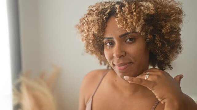 Woman touching cheek with hand, bra strap visible in studio closeup portrait with soft natural light; calm confidence.