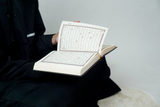 Young Muslim child holding an open Quran during Islamic learning session indoors. Religious education concept.