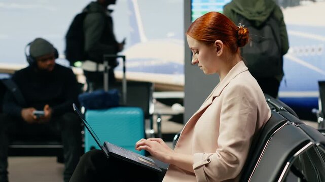 A general manager types on a laptop and puts on earbuds in an airport lounge, handling work tasks while waiting for a business flight.