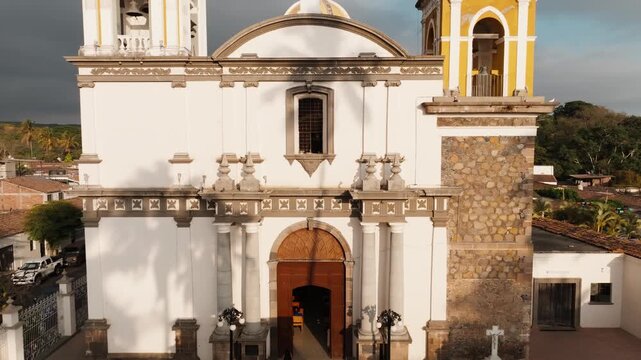 Ascending aerial view of the facade of Parroquia de San Miguel Arc&aacute;ngel in the historic center of Comala, Colima, Mexico revealing the iconic twin bell towers and the central dome