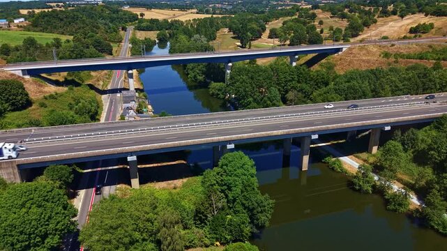 Autoroute L'Armoricaine motorway bridge carries moving traffic across the Mayenne River at Change, Mayenne, Pays de la Loire, France, beside a secondary road bridge, slow drone forward flyover.