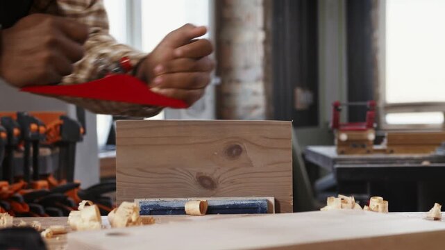 Craftsman smoothing solid wood block with hand plane, producing curled wood shavings while refining timber surface on workbench in woodworking workshop