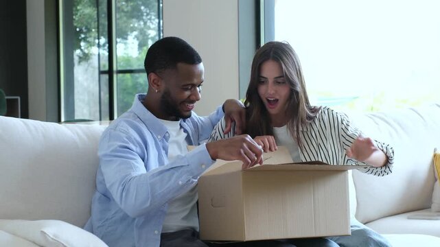 A happy diverse couple eagerly unboxes a surprise package delivered to their modern home, showcasing the joy of online shopping and receiving new purchases together.