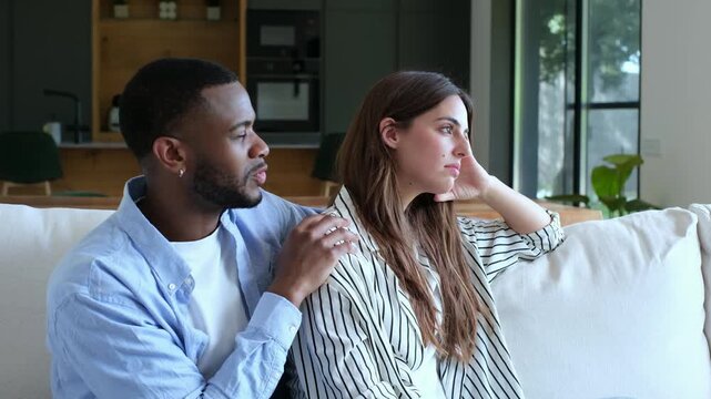 Empathetic african american man comforting his despondent caucasian girlfriend, offering emotional support by gently touching her shoulder while she looks away with a sad expression	
