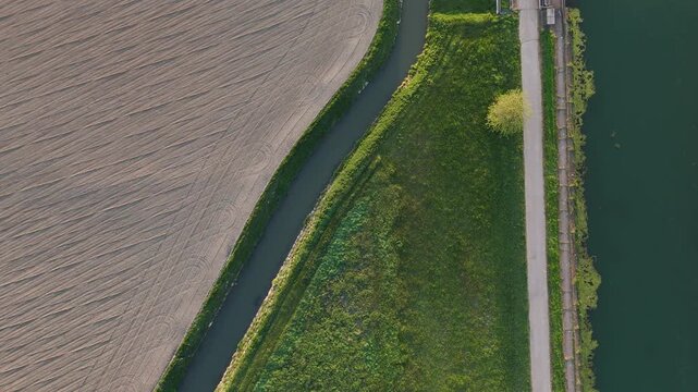 Milano-Cremona-Po Canal runs beside a smaller irrigation channel and farmland near Spinadesco, Cremona, Lombardy, Italy, across the Po Valley, top down drone slide.