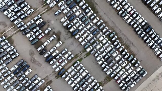 Hundreds of new passenger cars fill a vast vehicle storage and distribution lot in dense organized rows, highlighting automotive inventory and logistics, top down drone ascent.