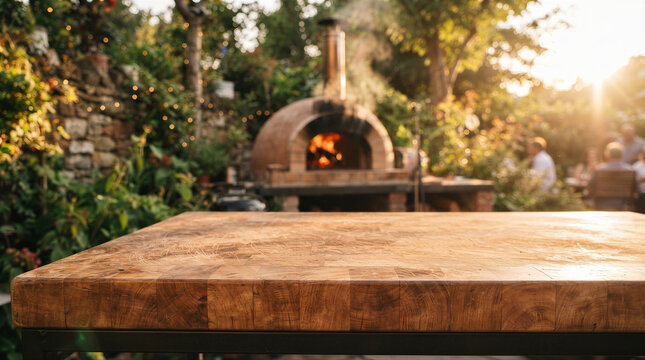Empty wooden table surface in a rustic outdoor garden setting with a woodfired pizza oven in the background at sunset