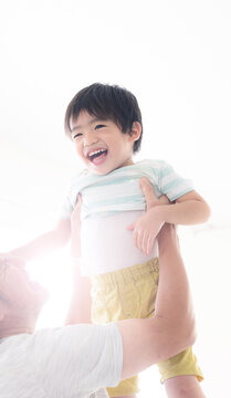 逆光の中子どもを高い高いをして、抱っこして遊ぶグレイヘアの祖父 孫とのふれあい・育児や子育て、成長の明るいイメージ	