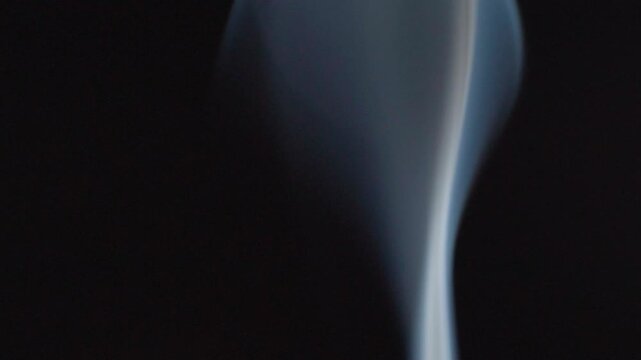 Macro closeup of white incense smoke flowing against black background in slow motion. Delicate abstract movement creating soft curves for meditation and wellness concepts