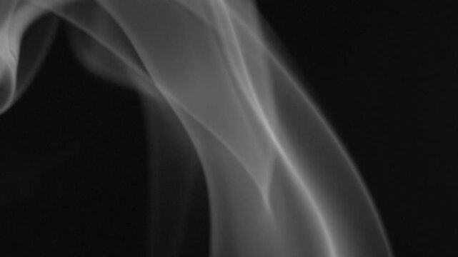 White incense smoke rising gently against black background in slow motion. Abstract flowing pattern creating peaceful atmosphere for meditation, relaxation, and wellness themes.