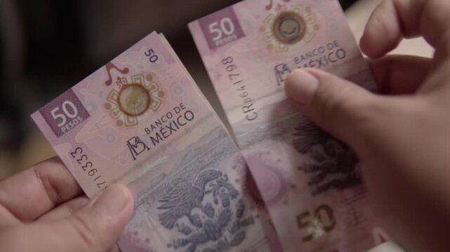 Closeup of hands counting Mexican peso banknotes during cash transaction. Person handling paper currency, illustrating finance, payment, budgeting, spending, and personal money