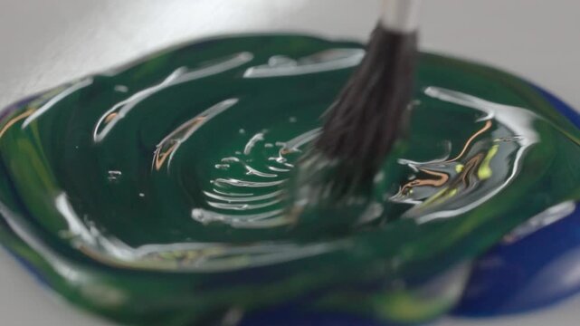 Close up of paintbrush mixing dark green acrylic paint with smooth flowing texture and glossy surface. Abstract artistic motion for creative painting and design concepts