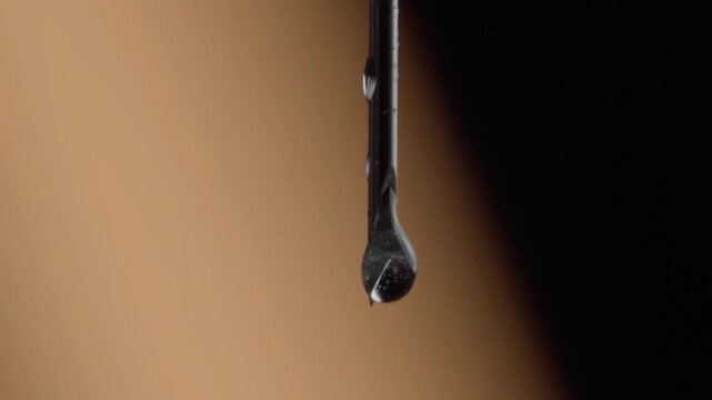 Extreme closeup of metal drill bit with water droplet forming on the tip. Detailed macro footage highlighting precision tool texture against soft blurred background