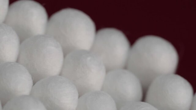 Pan left closeup of cotton swabs packed together with soft white cotton tips creating a clean repeating pattern against a red background. Everyday hygiene and personal care product