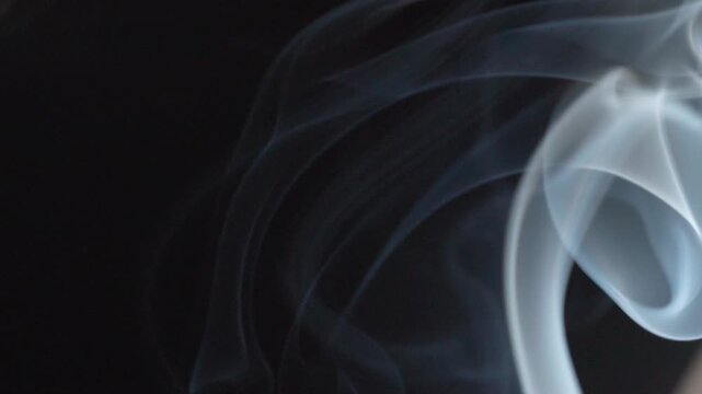 Abstract white incense smoke swirling through dark background, creating flowing patterns, soft curves and atmospheric motion in closeup.