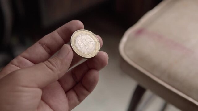 Hand holding a Mexican bimetallic coin in closeup against a blurred indoor background. Macro view highlights engraved details, metallic texture and circular design of the currency