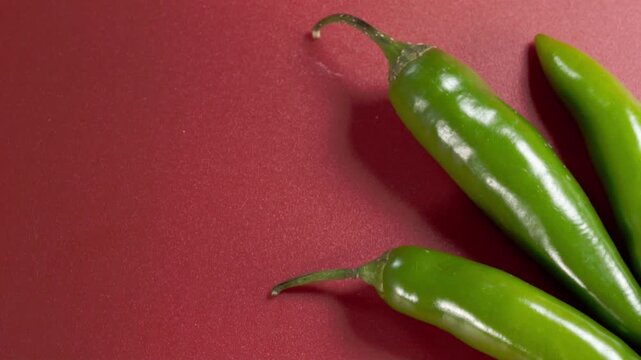 Extreme closeup of fresh green chili peppers arranged on red background, showcasing glossy surface, vibrant color and natural texture