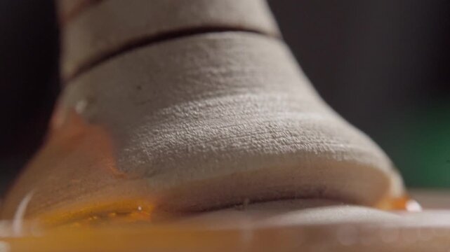 Macro closeup of thick honey flowing over a wooden honey dipper in slow motion. Golden honey coats the grooved surface, highlighting smooth texture, viscosity and natural sweetness.