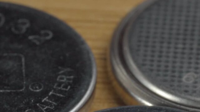 Extreme closeup of button cell batteries displaying engraved model numbers and worn metal surfaces. Macro view highlights circular shape, fine scratches and battery construction details